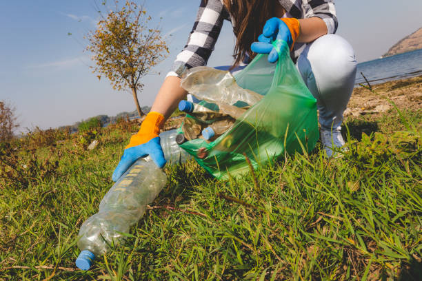 Female volunteer picking up plastic trash outdoors. Environment and save the earth concept. Close up of woman hand collecting plastic garbage bottle from the ground. Recycling and ecology concept. polyethylene terephthalate stock pictures, royalty-free photos & images