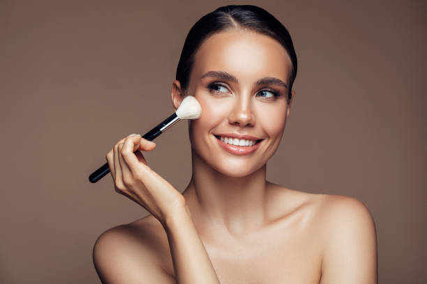 beautiful young woman applying foundation powder - face powder imagens e fotografias de stock