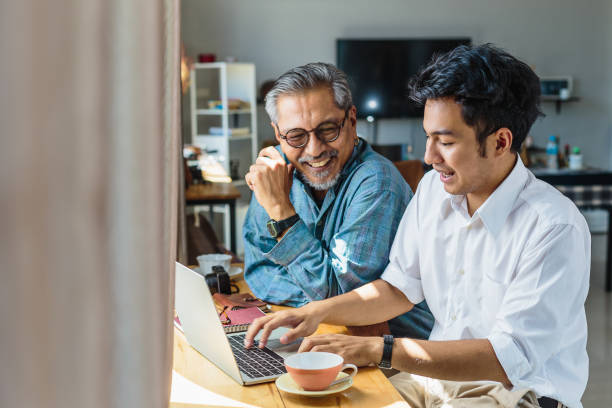 Asian senior father and his adult son using laptop computer while sitting at home Asian senior father and his adult son using laptop computer while sitting at home adults only stock pictures, royalty-free photos & images