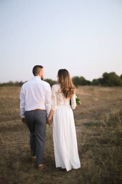 istock Bride and groom walking in field and holding hands 1186052611