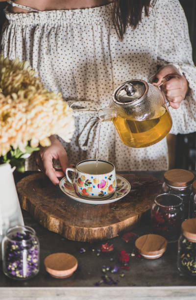 young woman pouring green tea from glass pot into cup - drinking tea cup drink imagens e fotografias de stock