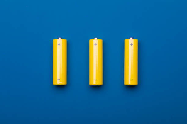 Top view of three yellow AA alkaline batteries (Mignons) or NiMH rechargeable cells on blue background