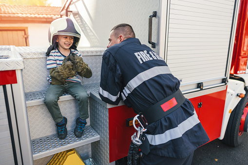 Little boy playing with firefighter helmet and gloves and talking with real firefighter