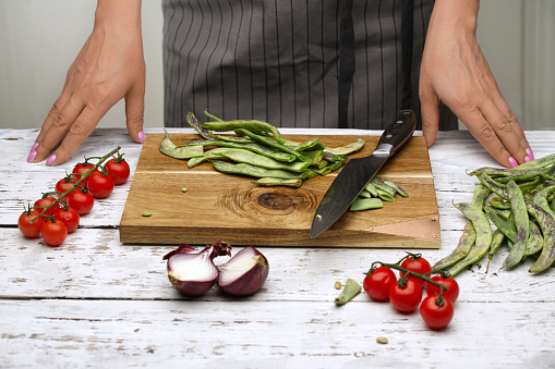 The chef prepares green beans, tomatoes on a branch, red onions in the white kitchen. wooden cutting Board on rustic background