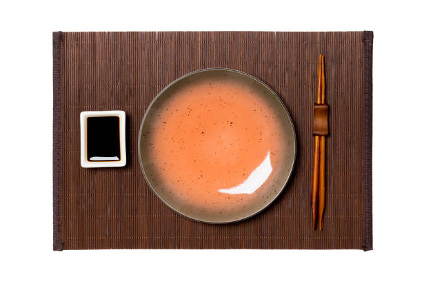 Empty round brown plate with chopsticks for sushi and soy sauce on dark bamboo mat background. Top view with copy space for you design.