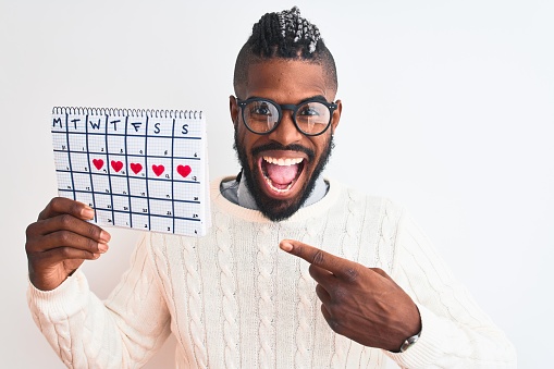 African american man with braids holding period calendar over isolated white background very happy pointing with hand and finger