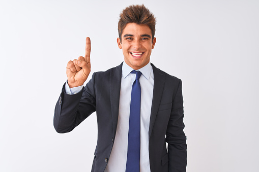 Young handsome businessman wearing suit standing over isolated white background showing and pointing up with finger number one while smiling confident and happy.