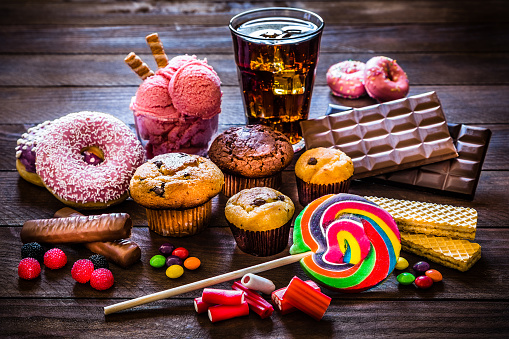 Assortment of products with high sugar level like candies, gummy candies, donuts, soda, chocolate, lollipop, wafers and cupcakes on rustic wooden table. Low key DSLR photo taken with Canon EOS 6D Mark II and Canon EF 24-105 mm f/4L