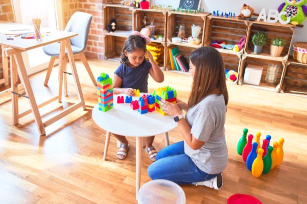 schöne lehrerin und kleinkind mädchen spielen mit baublöcken bulding turm im kindergarten - child playroom parent indoors stock-fotos und bilder