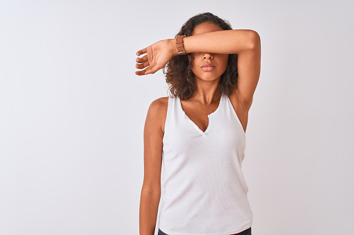 Young brazilian woman wearing casual t-shirt standing over isolated white background covering eyes with arm, looking serious and sad. Sightless, hiding and rejection concept