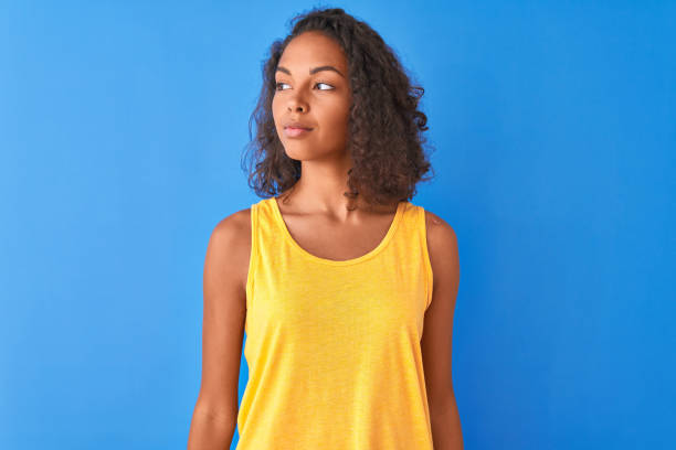 mulher brasileira nova que desgasta o t-shirt amarelo que está sobre o fundo azul isolado que sorri olhando ao lado e que olha afastado que pensa. - teenage girls ideas blue yellow - fotografias e filmes do acervo