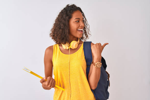 istock Brazilian student woman wearing backpack holding notebook over isolated white background pointing and showing with thumb up to the side with happy face smiling 1186064915
