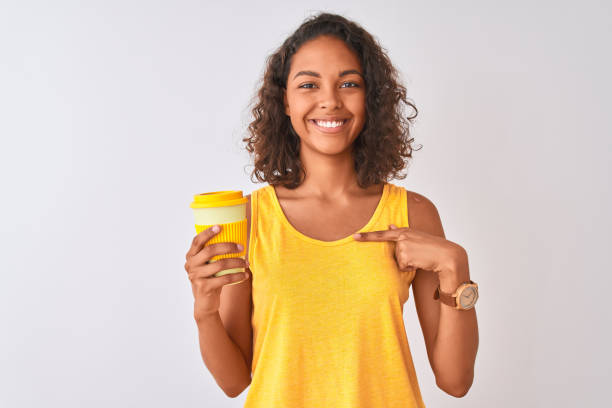 Young brazilian woman drinking take away coffee standing over isolated white background with surprise face pointing finger to himself