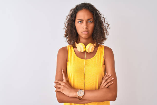 молодая бразильская женщина в желтых наушниках на изолированном белом фоне скептика и нервного, неодобрительного выражения на лице со скр� - arms crossed audio стоковые фото и изображения