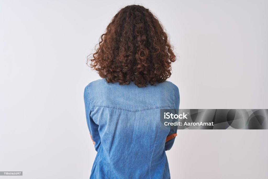 Young brazilian woman wearing denim shirt standing over isolated white background standing backwards looking away with crossed arms Rear View Stock Photo