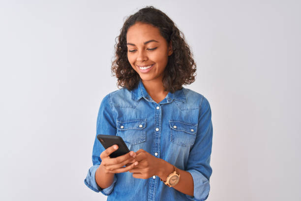 young brazilian woman using smartphone standing over isolated white background with a happy face standing and smiling with a confident smile showing teeth - teenager teenagers only one teenage girl only human face imagens e fotografias de stock