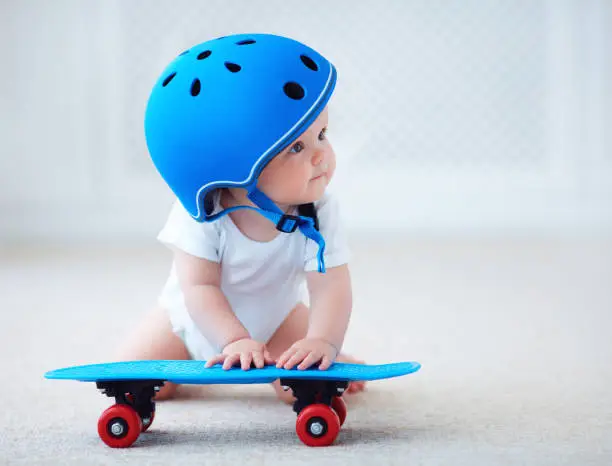 Photo of cute infant baby girl in protective helmet outfit ready to ride skateboard, extreme sport concept