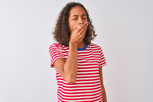 Joven mujer brasileña con camiseta de rayas rojas de pie sobre fondo blanco aislado aburrido bostezando cansado cubriendo la boca con la mano. Inquieto y tranquilo. photo