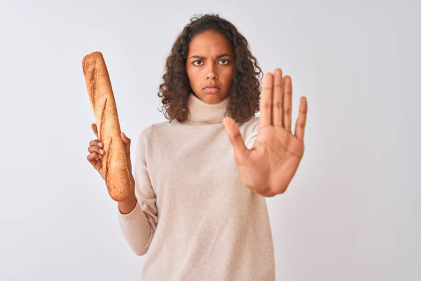 istock Young brazilian baker woman holding bread standing over isolated white background with open hand doing stop sign with serious and confident expression, defense gesture 1186067093