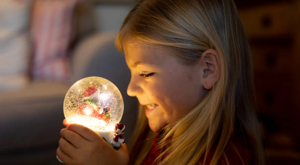 Girl at home at Christmas time Side view close up of a young Caucasian girl holding a snow globe in the sitting room at Christmas time, smiling snow globe photos stock pictures, royalty-free photos & images