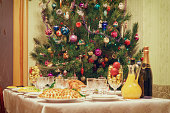 Served table with festive dishes near beautiful decorated Christmas tree in living room interior. Concept of new year holiday at cozy home. Focus on fir, vintage tone