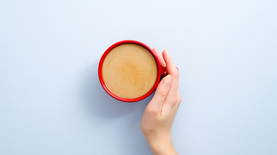 Female hand holding latte coffee cup on blue background. Flat lay, top view, overhead.
