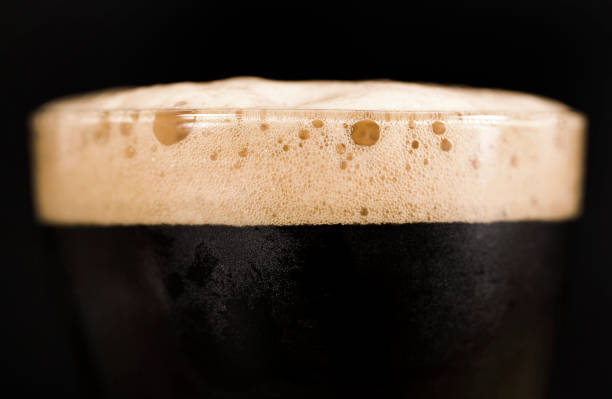 Glass of dark beer with foam Glass of dark beer isolated on black background. Foam close up. porter photos stock pictures, royalty-free photos & images