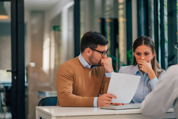 Portrait of a couple with financial problems looking at document in financial adviser's office. Portrait of a couple with financial problems looking at document in financial adviser's office. mortgage document photos stock pictures, royalty-free photos & images