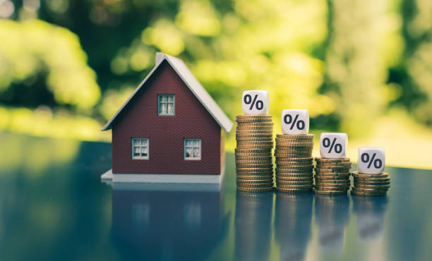 Symbol for decreasing interest rates. Dice with percentage symbols on decreasing high stacks of coins next to a model house. stock photo