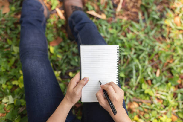 istock close up hand young man are sitting using pen writing Record Lecture notepad into the book in the park. top view 1186083472
