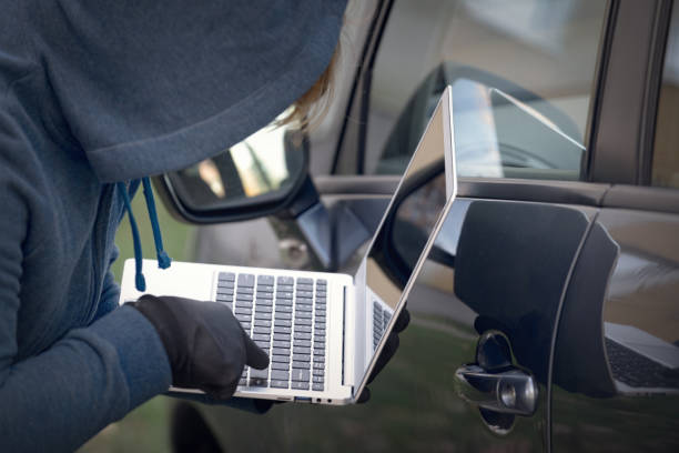 złodziej z kapturem próbuje złamać systemy bezpieczeństwa samochodu z laptopem. - disarmament zdjęcia i obrazy z banku zdjęć