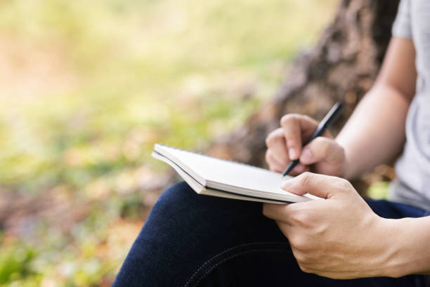 istock close up hand young man are sitting using pen writing Record Lecture notepad into the book in the park. 1186083651
