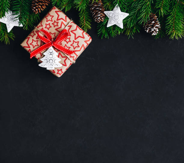istock Christmas background with fir branches and a gift box with a red bow on a dark concrete background. 1186086338