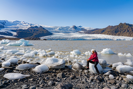 nice senior woman on the shore of Jokulsarlon glacier lagoon with Vatnajokull glacier in the background