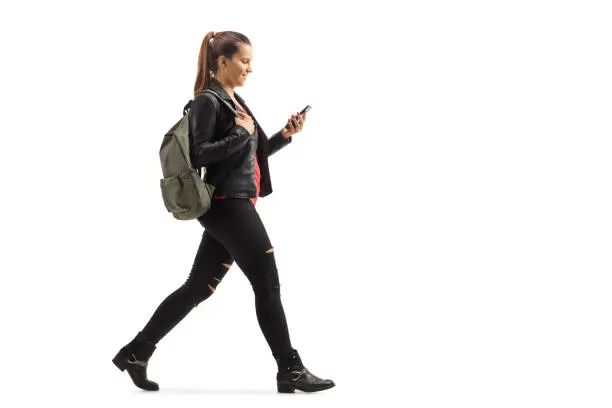 Photo of Girl with a backpack walking and looking at her mobile phone