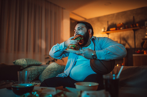 Hombre viendo un partido deportivo y comiendo hamburguesa photo
