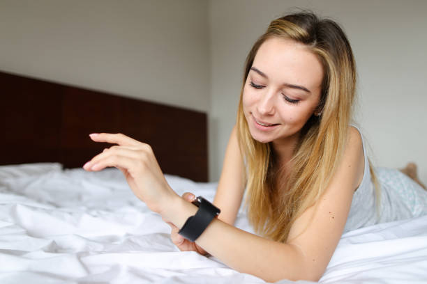 istock Young girl lying on bed with smart watch, white linens background 1186101459