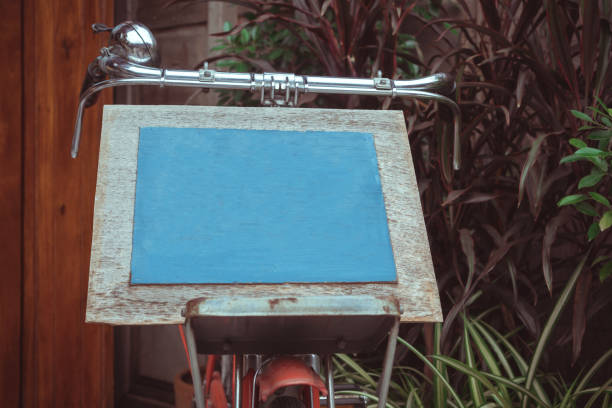 Mock up blank board advertising billboard for wood frame on old bicycle at front restaurant cafe garden tree background, display your product insert  text. retro vintage decoration style