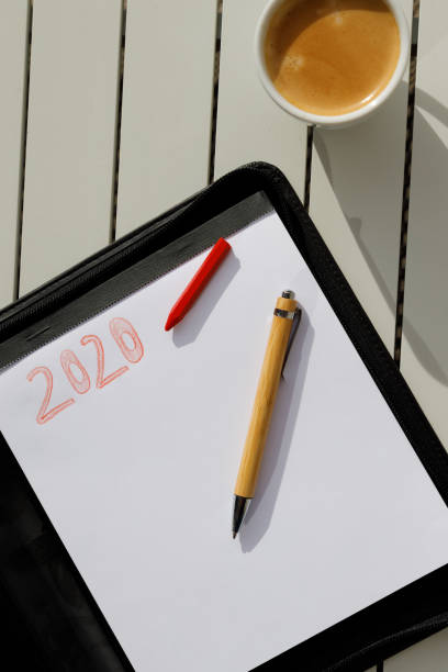 istock Pen and red pencil on white sheet with the title 2020, on table with coffee next to it. New Year's Purposes. 1186107722
