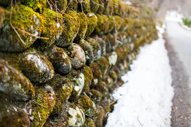 Abstract closeup of stone wall in Okuhida villages near Takayama, Japan mountain in Gifu Prefecture park with moss and snow by road