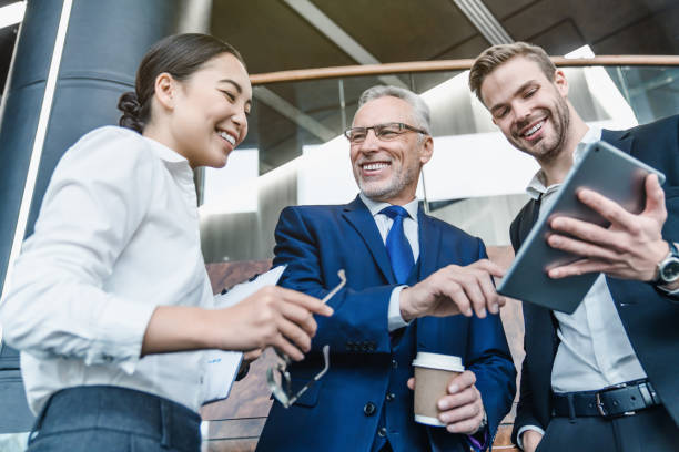 Low angle view of group successful business people in suits using digital tablet indoor