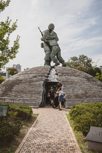Seoul, South Korea - September 26, 2019: Visitors to Seoul's War Memorial of Korea step through a crack symbolizing the division of Korea and into the dome underneath The Statue of Brothers. The statue depicts a scene where an older brother, an ROK officer, and his younger brother, a North Korean soldier, meet in a battlefield and express reconciliation, love, and forgiveness.