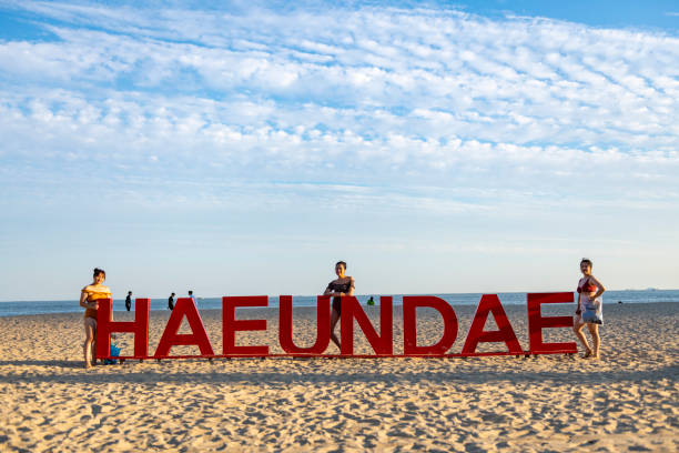 Busan, South Korea - September 18, 2019: Three tourists from Taiwan finish their day at the beach in Busan with a stop at a popular photo-op location -- a large sign with the name of the beach, Haeundae Beach.