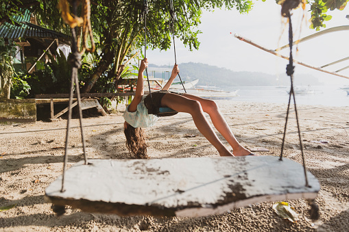 A young woman traveling in the Philippines enjoys a beach swing and the view from upside down in Port Barton, Palawan