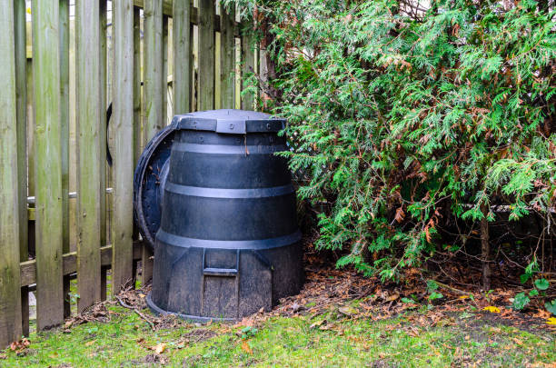 Backyard composter next to a fence and hedge