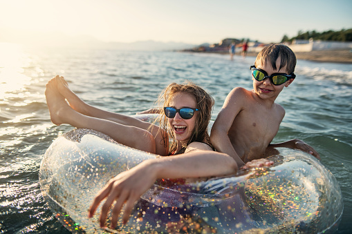 Kids are splashing and having fun on swim ring floating on the sea. Brother and sister are trapped together in a floating ring.\nNikon D810