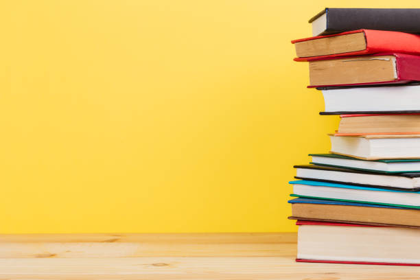 istock Simple Simple composition of many hardback books, unprocessed books on a wooden table and a yellow background. back to school. Copy space. Education. 1186122362