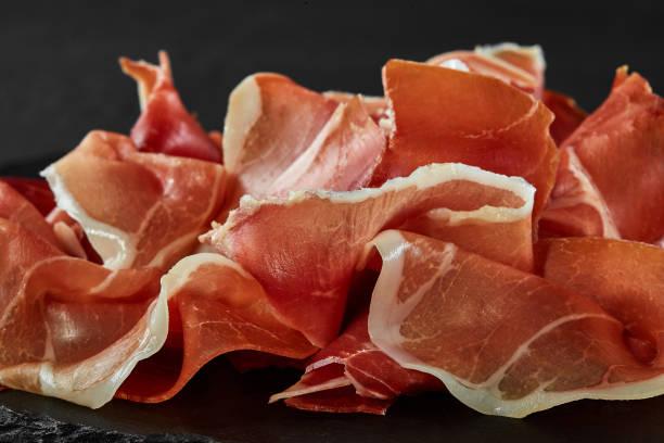 istock Gourmet, manually sliced jamon on black stone slate board against a dark grey background. Close-up shot. Side view. Copy space 1186122703
