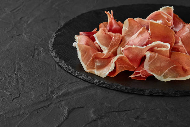 istock Gourmet, manually sliced jamon on black stone slate board against a dark grey background. Close-up shot. Side view. Copy space 1186123139
