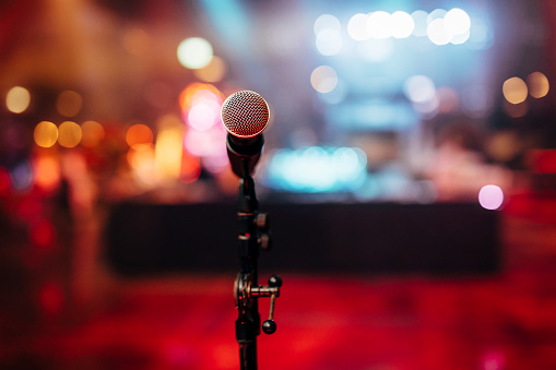 MIC ON A STAGE READY FOR THE SINGER OR SPEAKER WITH BLURRED BCKGROUND AND COLOUR BACK.